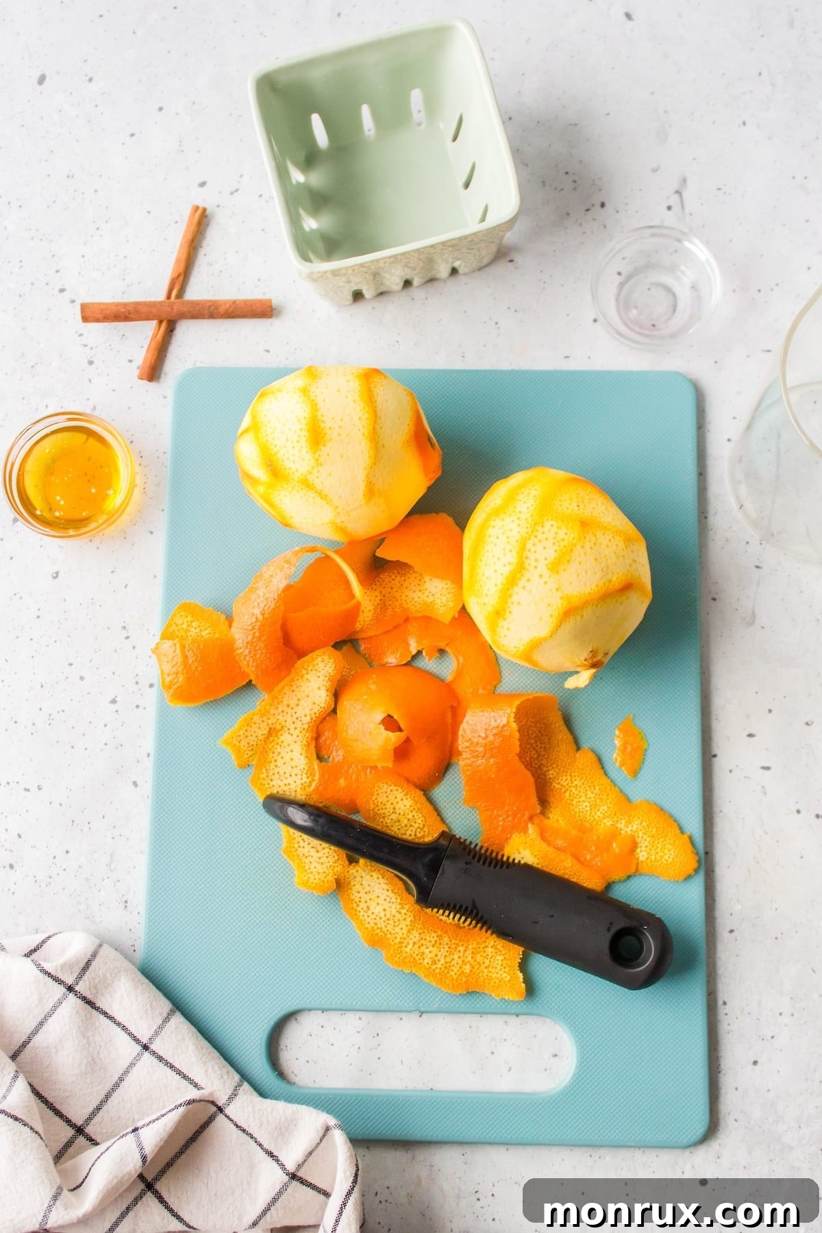 Two organic oranges are shown being peeled on a clean wooden cutting board, with strips of orange zest visible.
