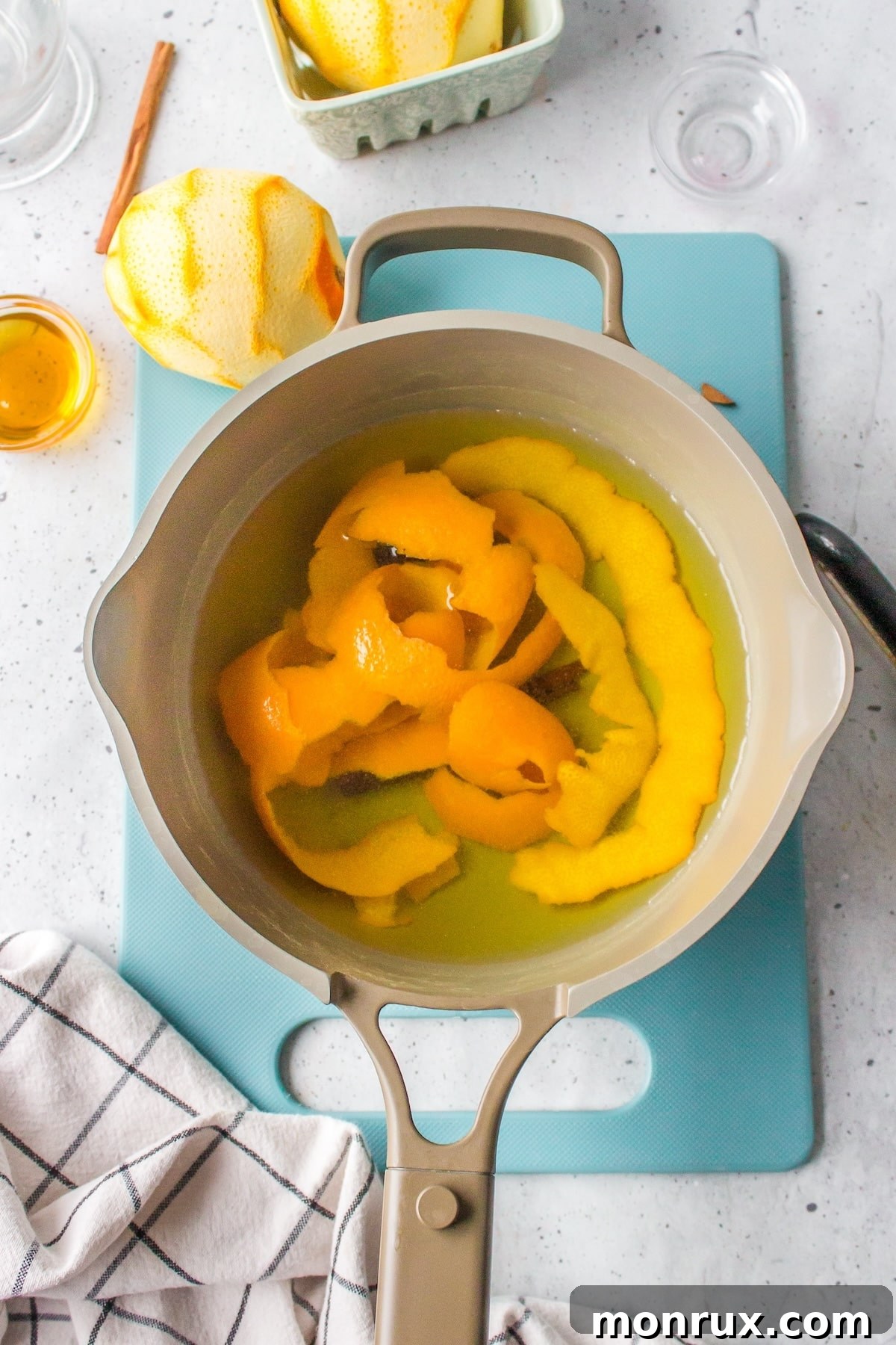 Close-up of orange peels and a cinnamon stick simmering gently in hot water within a stainless steel pot.