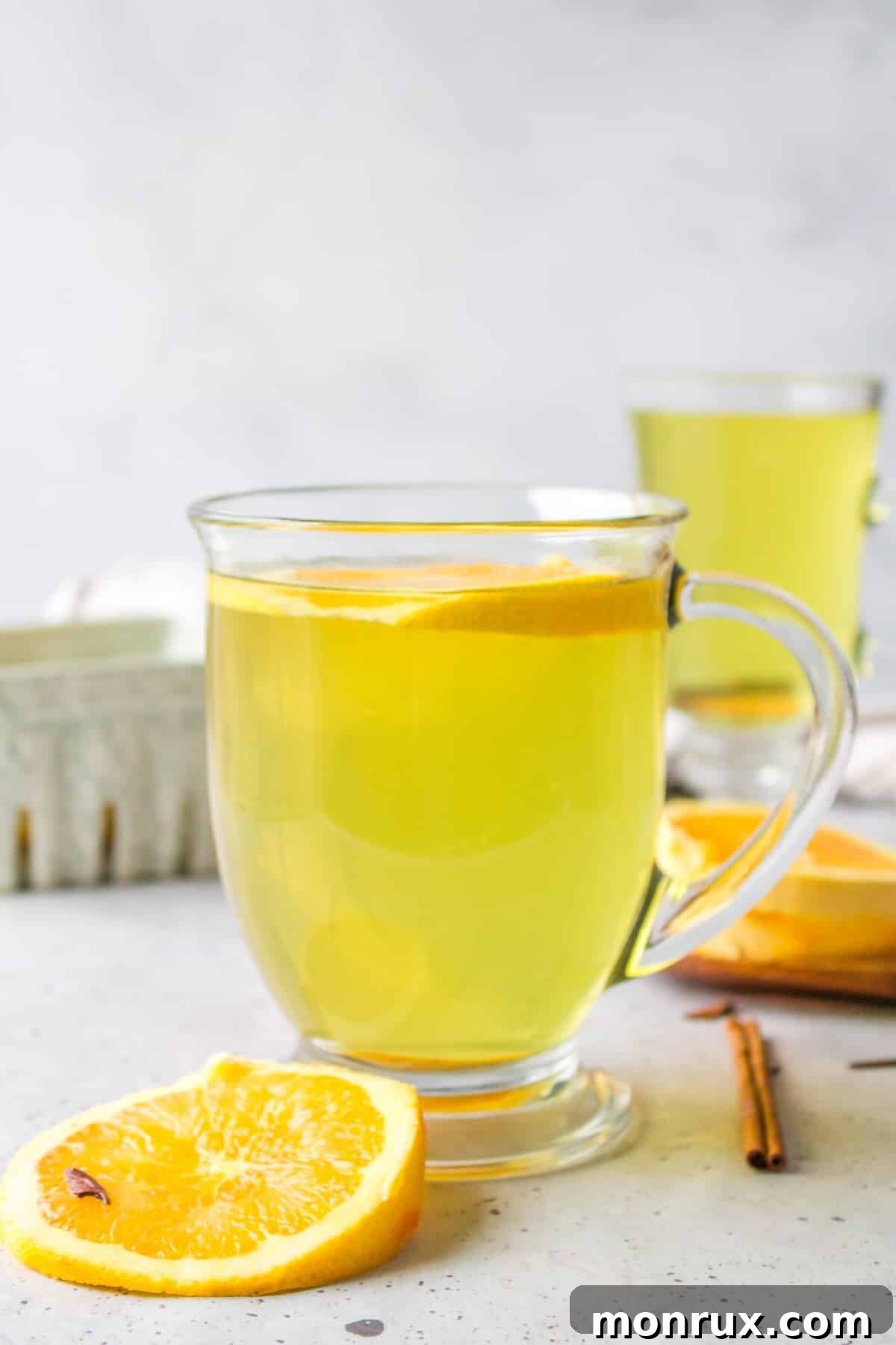 A side view of a glass mug filled with orange peel tea, featuring an orange slice garnish and a gentle steam rising from the hot beverage.