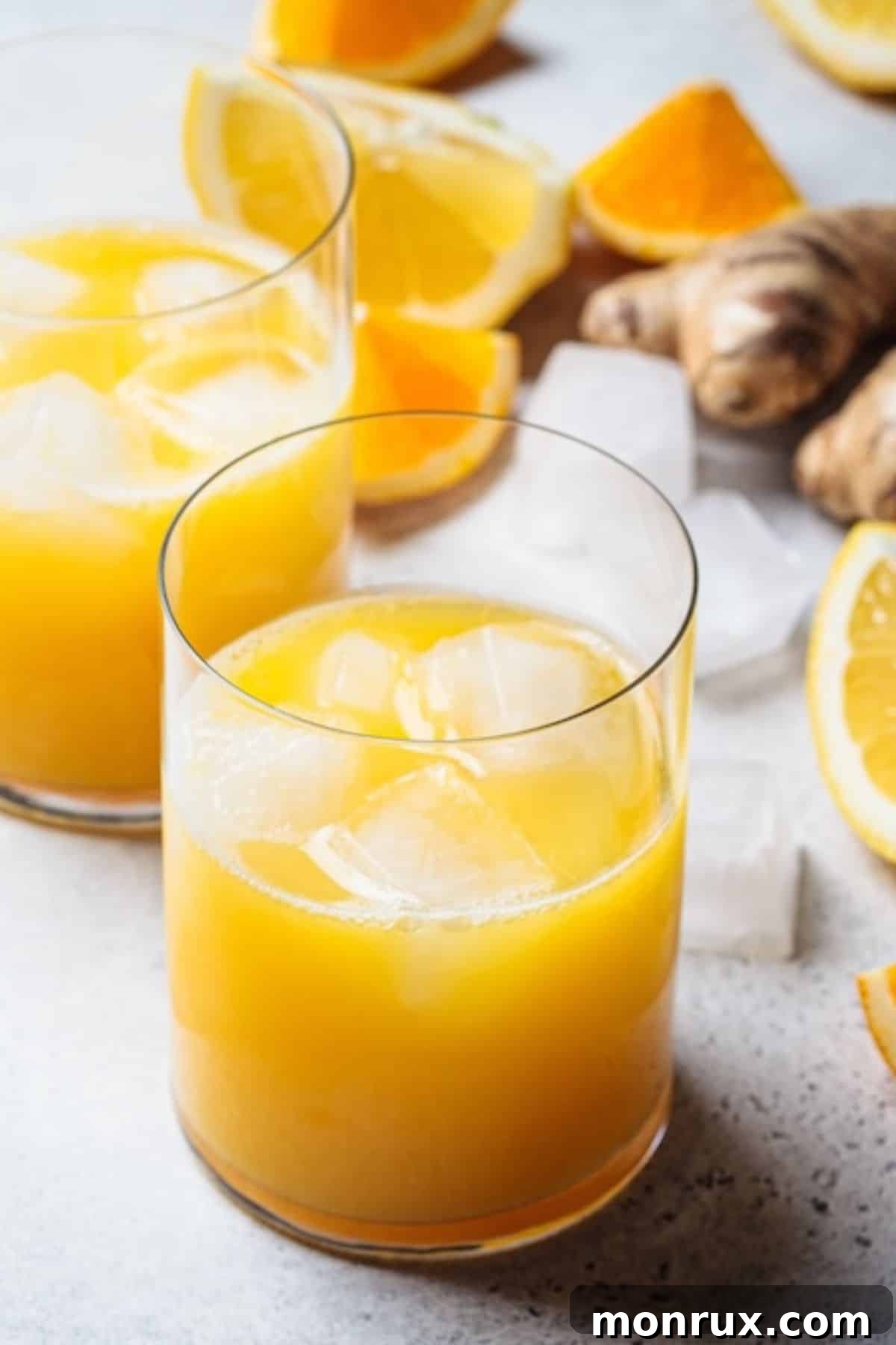 A refreshing glass of orange lemon ginger juice with ice and a mint garnish.