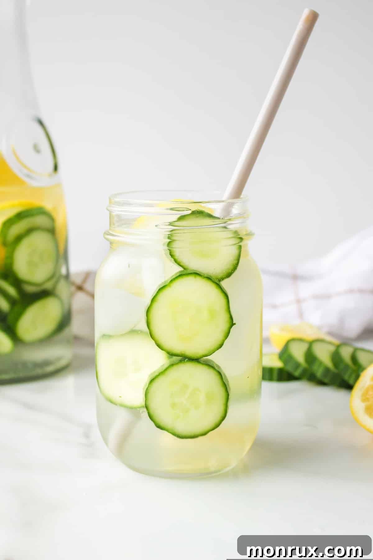 Refreshing cucumber spa water with ice and a paper straw, garnished with fresh cucumber slices.
