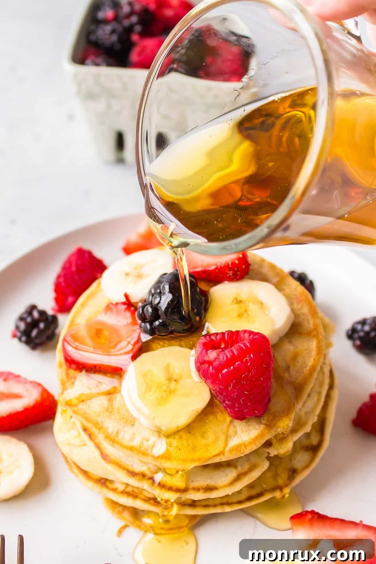 A delectable stack of golden-brown pancakes, generously drizzled with maple syrup and garnished with an abundance of fresh, ripe fruit, inviting you to indulge in a delightful breakfast.
