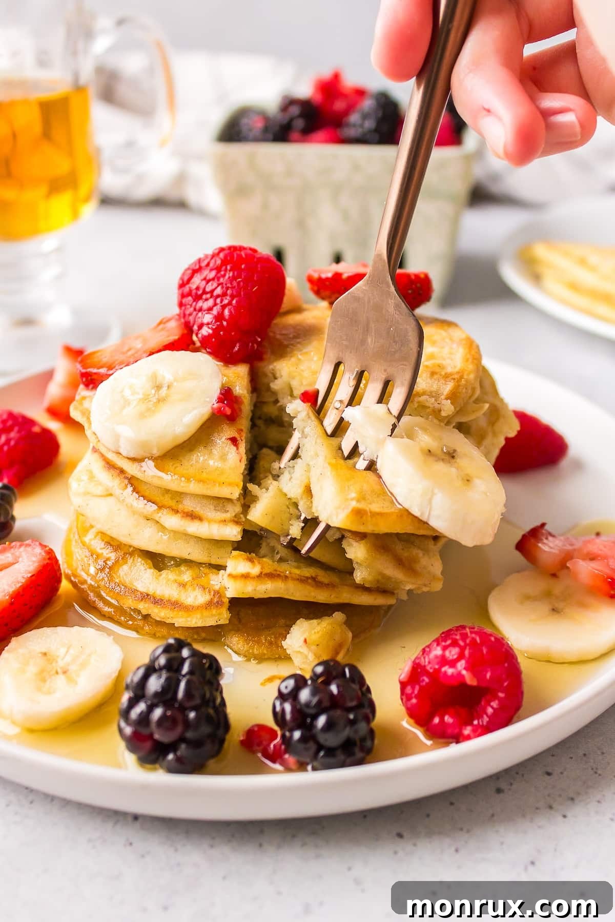 A close-up shot of a fork holding a delicious bite of pancake, complete with syrup and a piece of fresh fruit, highlighting the fluffy texture and appealing presentation.