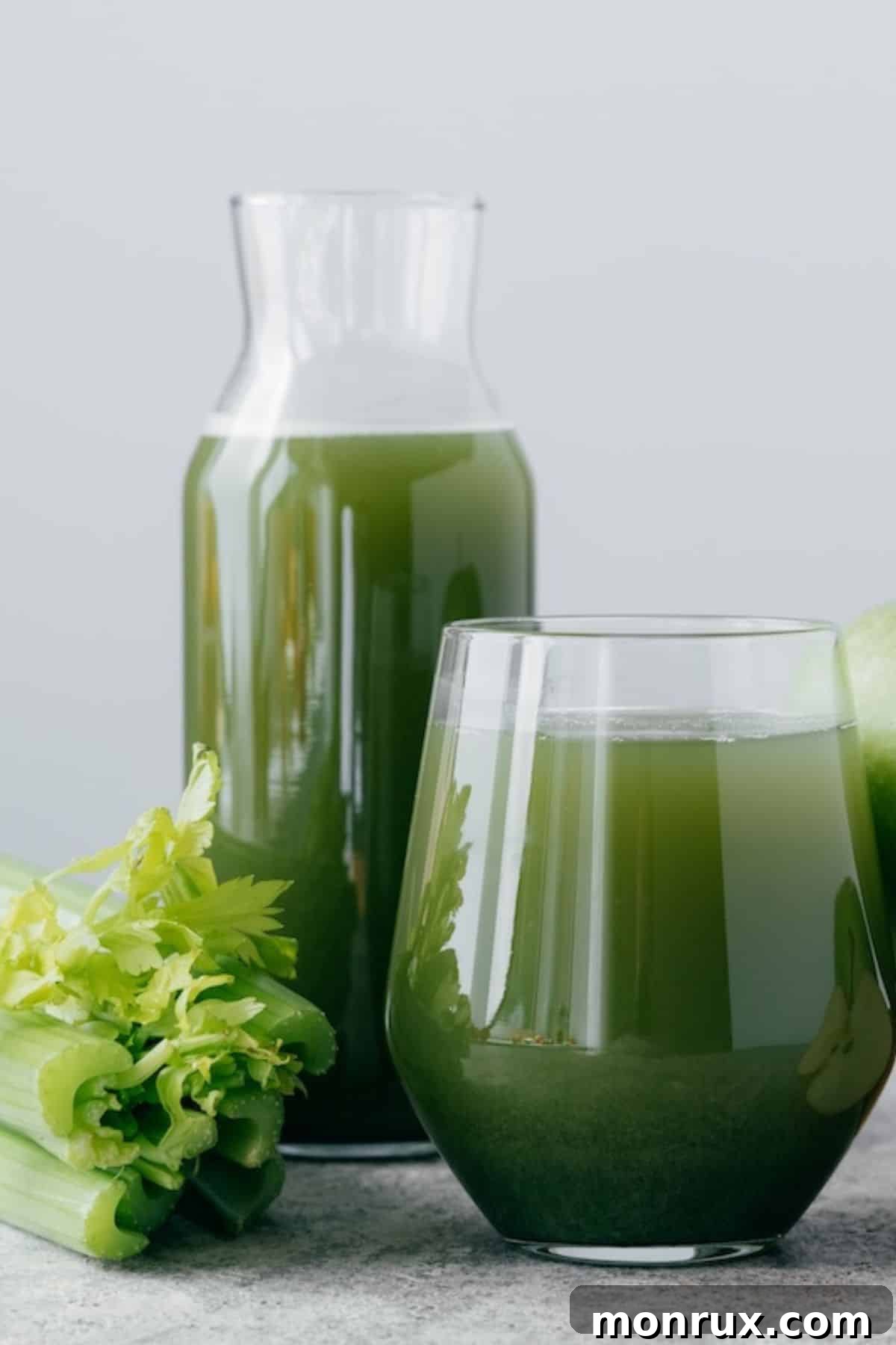 Green juice in a pitcher and glass on a table with fresh fruits, symbolizing detox and cleansing.