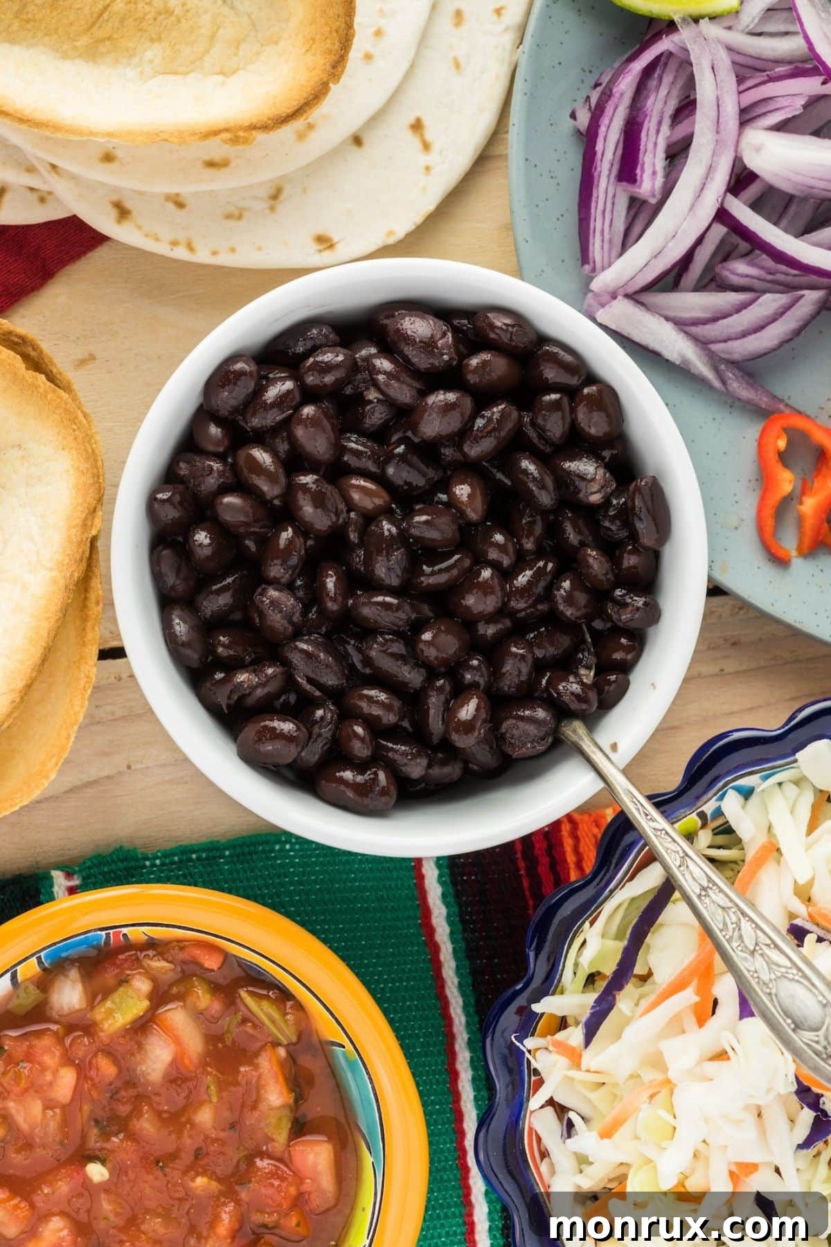A vibrant bowl of black beans, surrounded by fresh ingredients like bell peppers, cilantro, and limes, suggesting their versatile use in various culinary creations.