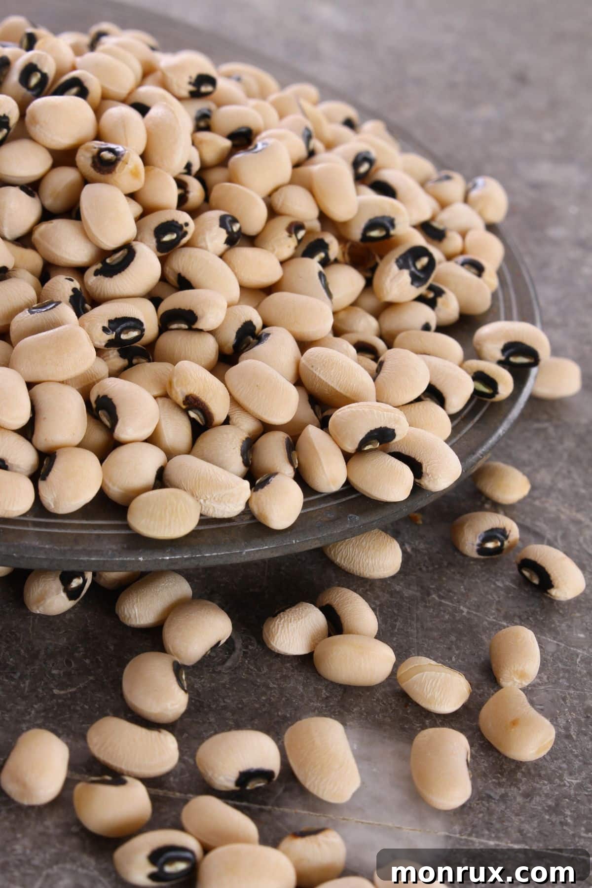 A close-up shot of black-eyed peas, some scattered on a plate and others spilling from it, highlighting their creamy color with the characteristic black 'eye'.