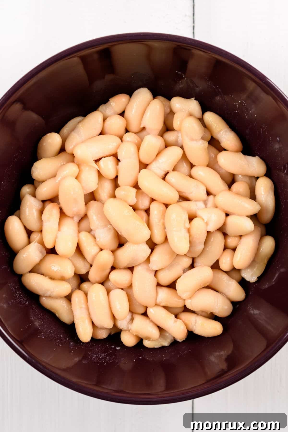 A rustic brown bowl filled with an abundance of creamy white beans, ready for cooking or serving.