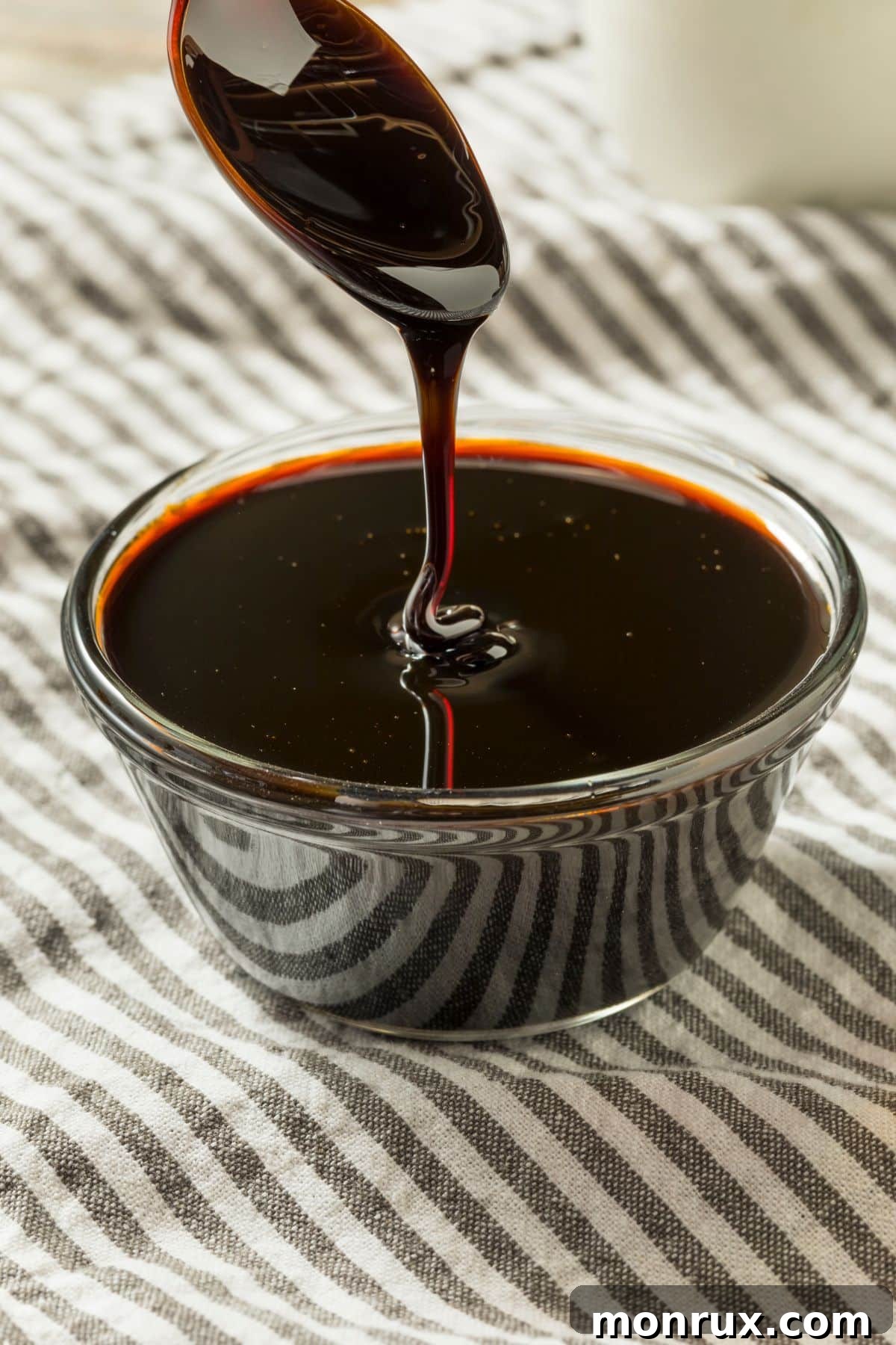 A close-up of thick, dark molasses being poured from a jar with a spoon, showing its viscous texture and rich color.