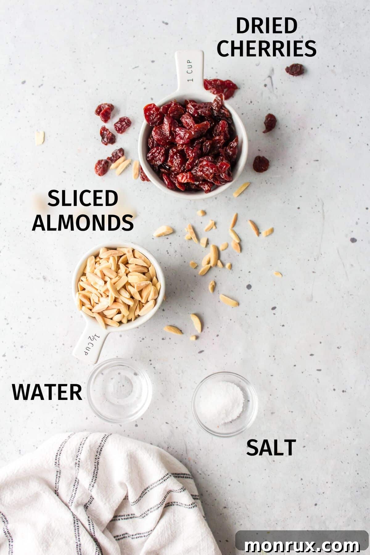 Fresh ingredients laid out on a white countertop: dried cherries, sliced almonds, and a sprinkle of sea salt.