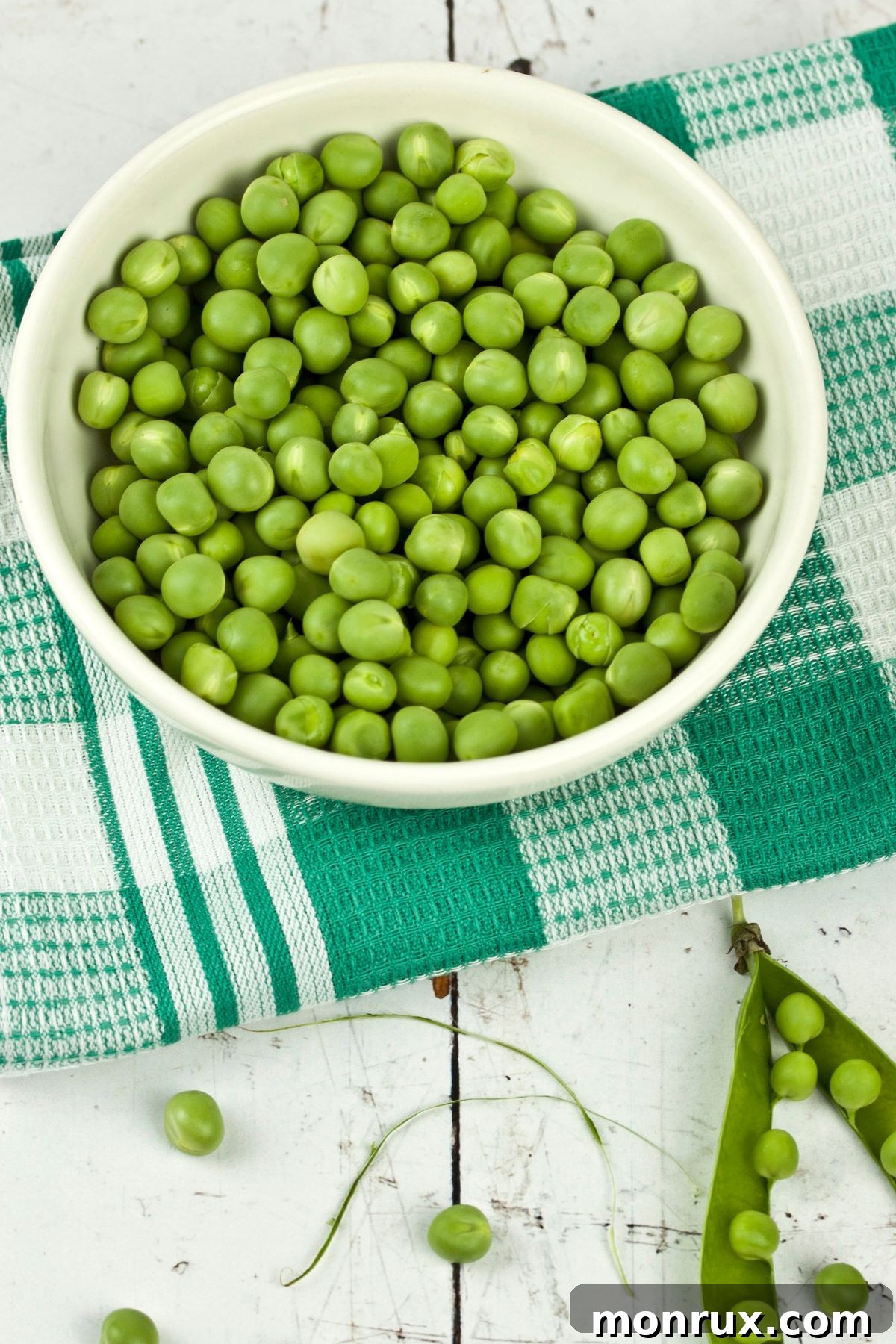 bowl of green peas on table with checkered towel.