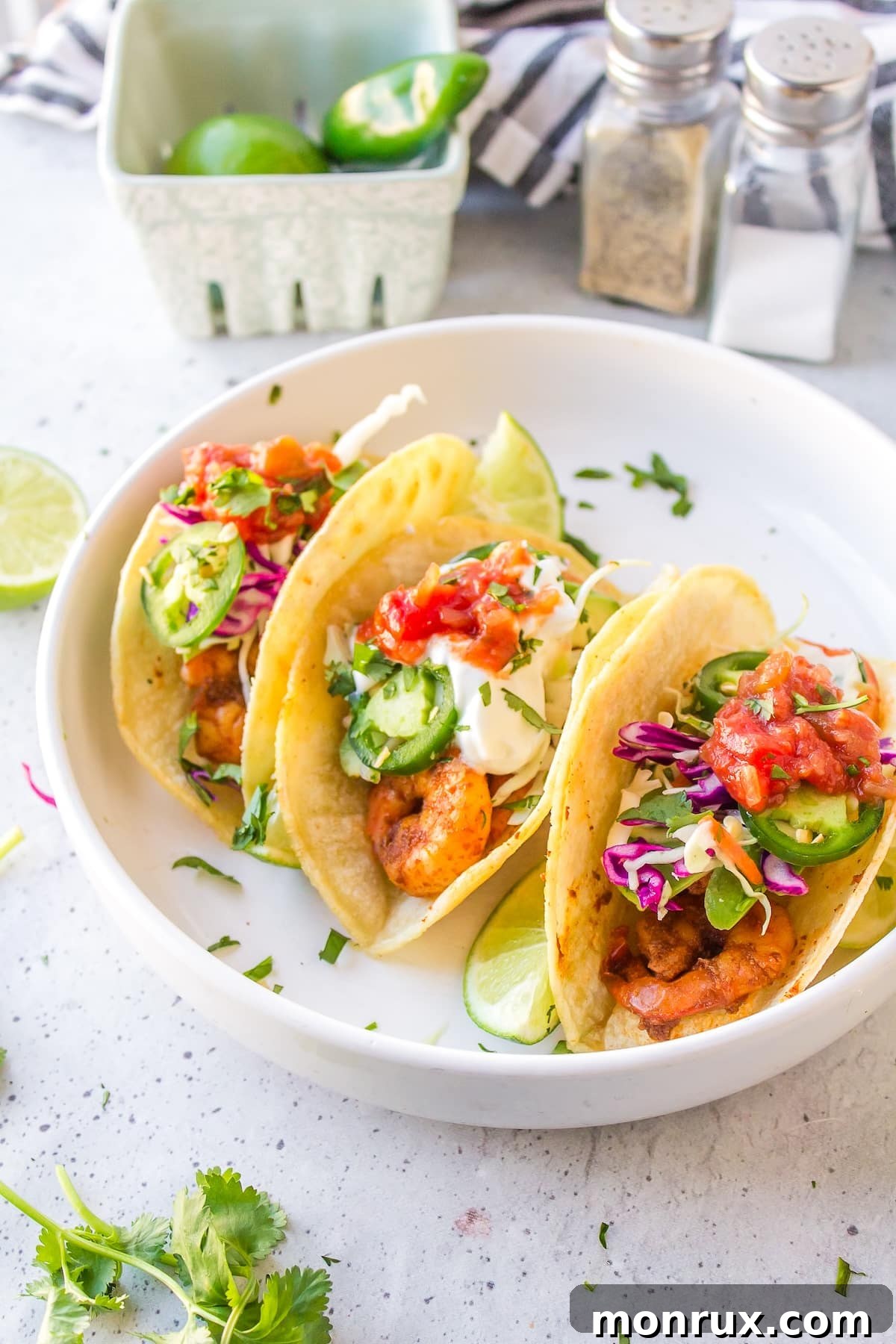 Three perfectly assembled Baja Shrimp Tacos on a white plate, garnished with fresh cilantro and a lime wedge.