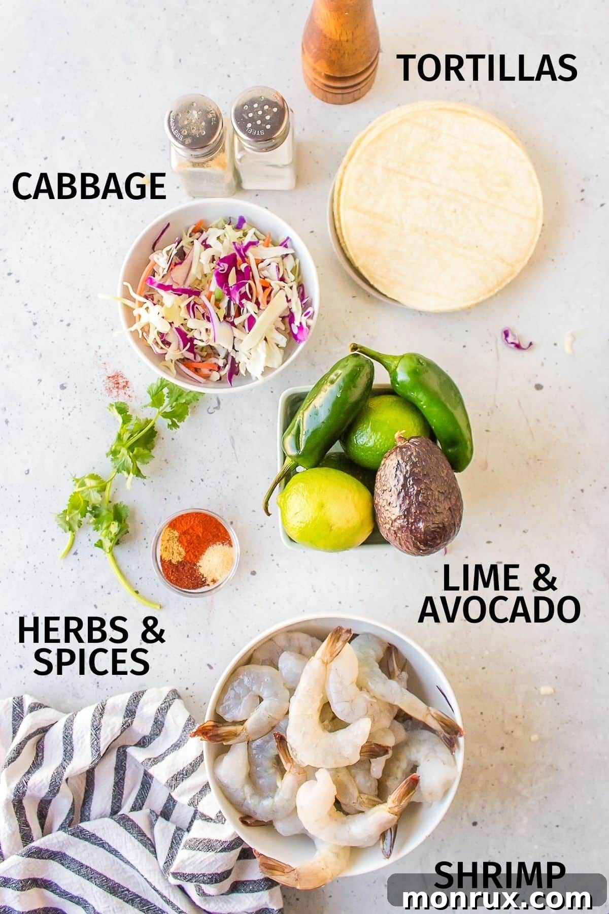 A selection of fresh ingredients laid out on a white countertop, including shrimp, cabbage, cilantro, limes, and spices, ready for making Baja Shrimp Tacos.