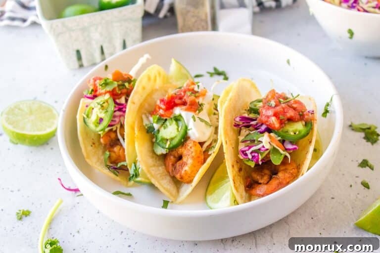 Three perfectly assembled Baja Shrimp Tacos on a white plate, garnished with fresh cilantro and a lime wedge.