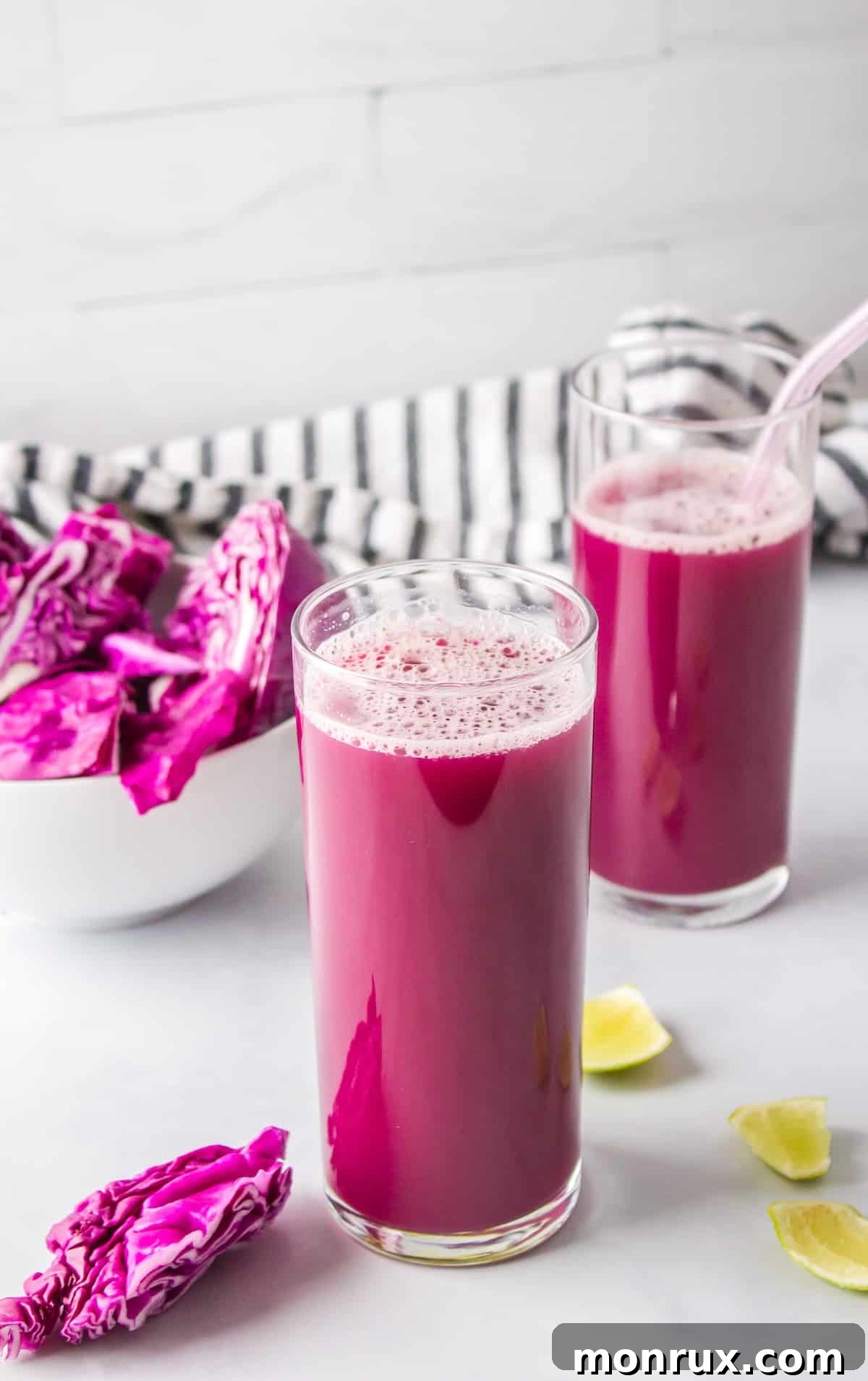 Two glasses of purple cabbage juice on a table, garnished with a lime slice.