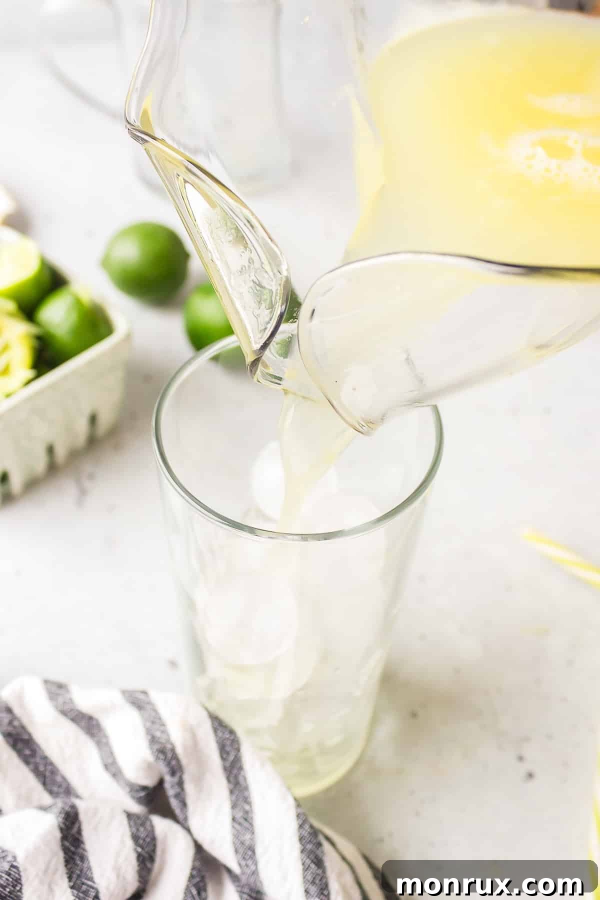 A hand elegantly pouring the vibrant, mixed ginger beer mocktail over perfectly sculpted ice cubes in a tall, frosty glass.