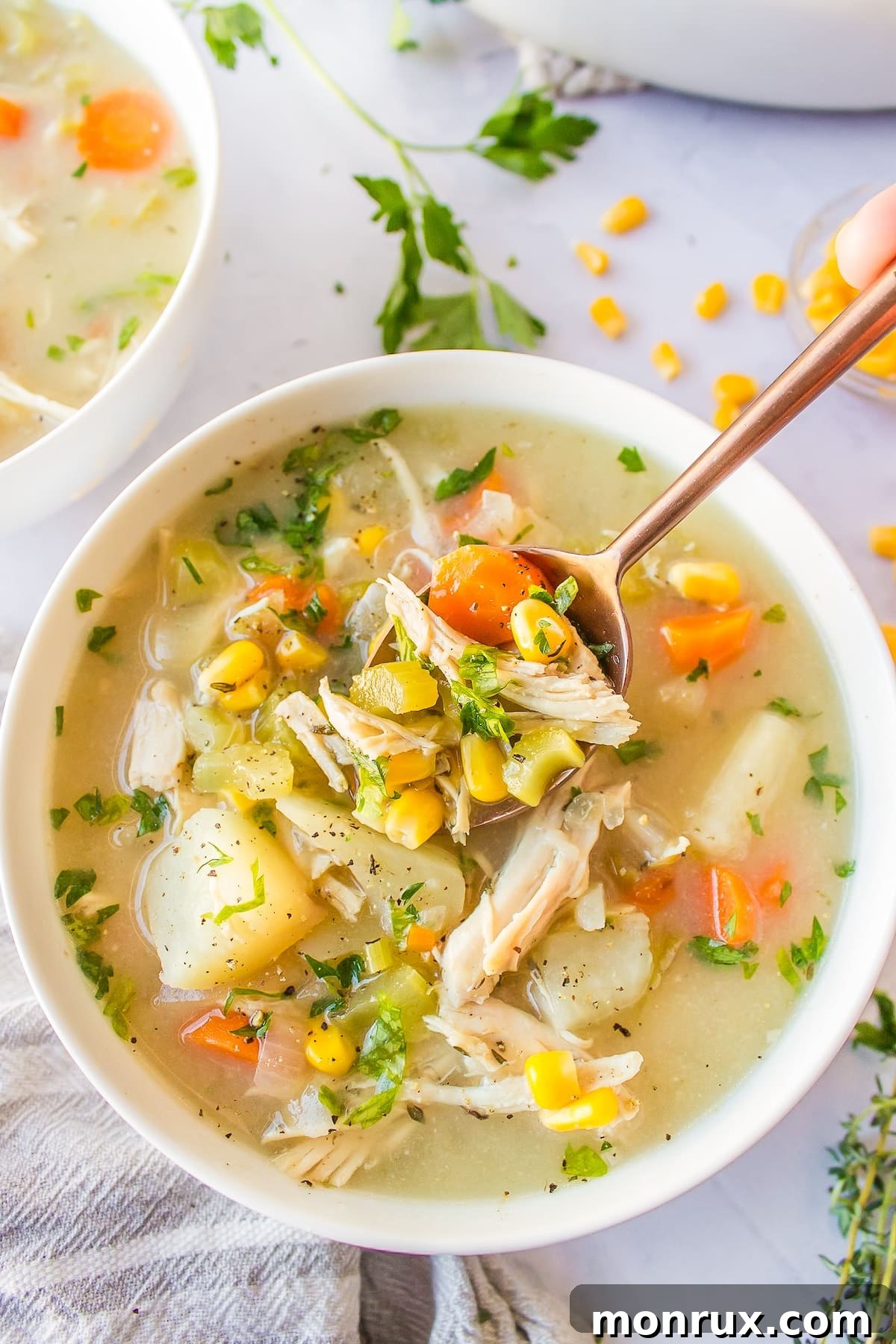A steaming bowl of creamy crockpot chicken, corn, and potato soup, garnished with fresh herbs.