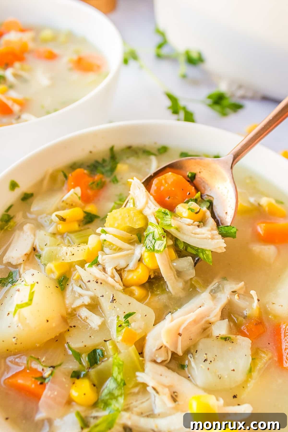 A spoonful of creamy chicken, corn, and potato soup being lifted from a bowl, showcasing its rich texture.