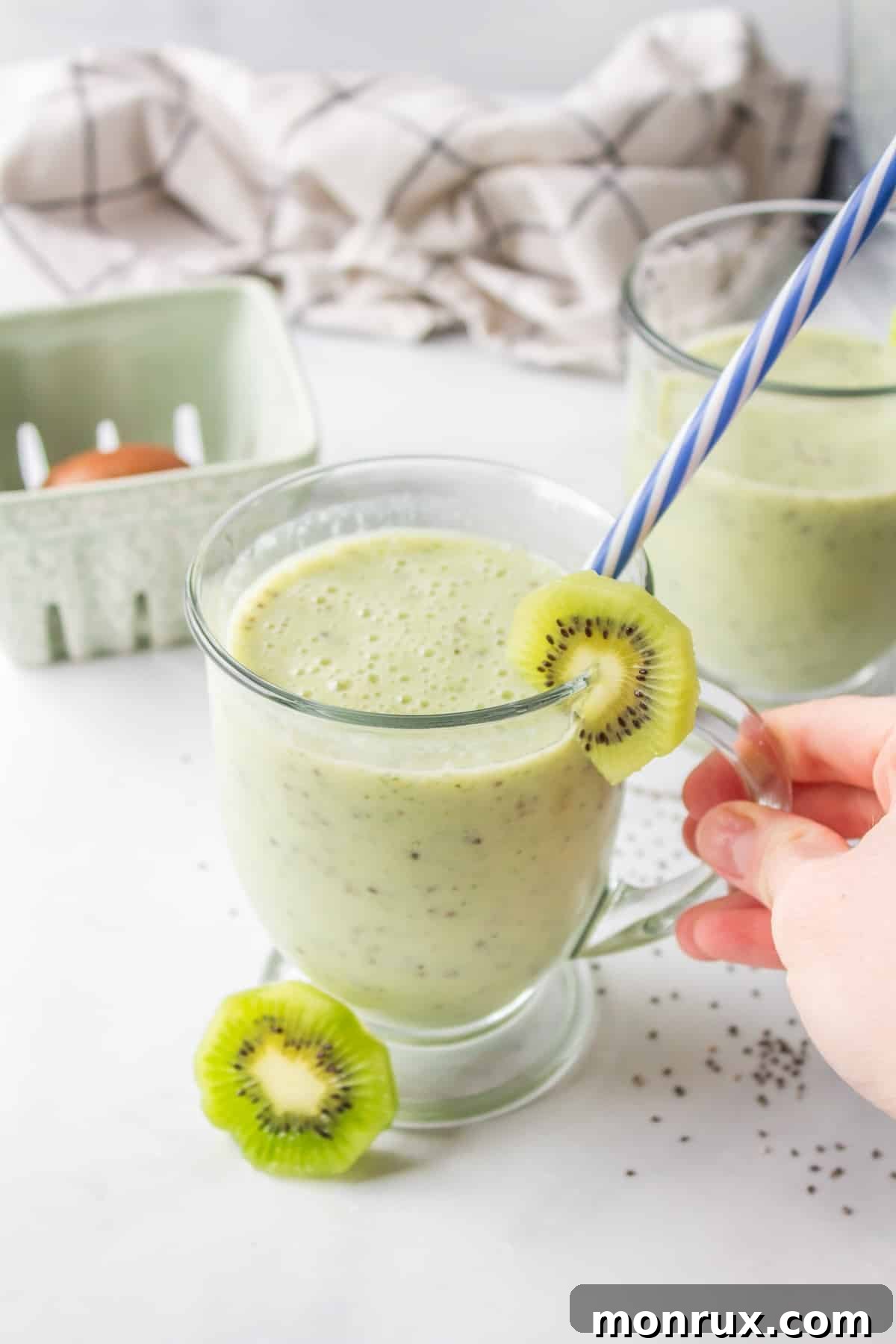 A glass of a vibrant green kiwi smoothie, garnished with fresh kiwi slices and a straw, ready to be enjoyed.