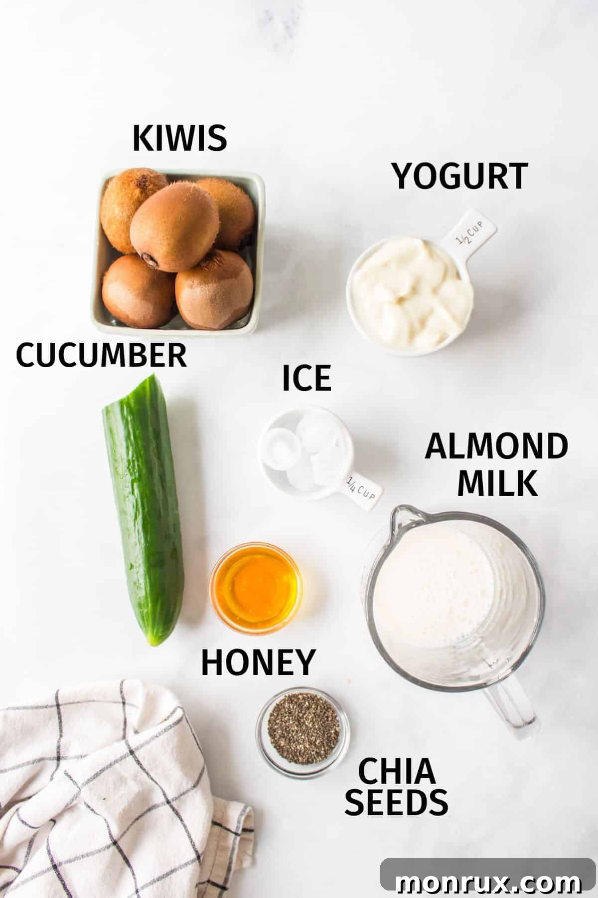 A selection of fresh ingredients including kiwis, cucumber, spinach, almond milk, Greek yogurt, and chia seeds laid out on a kitchen counter.