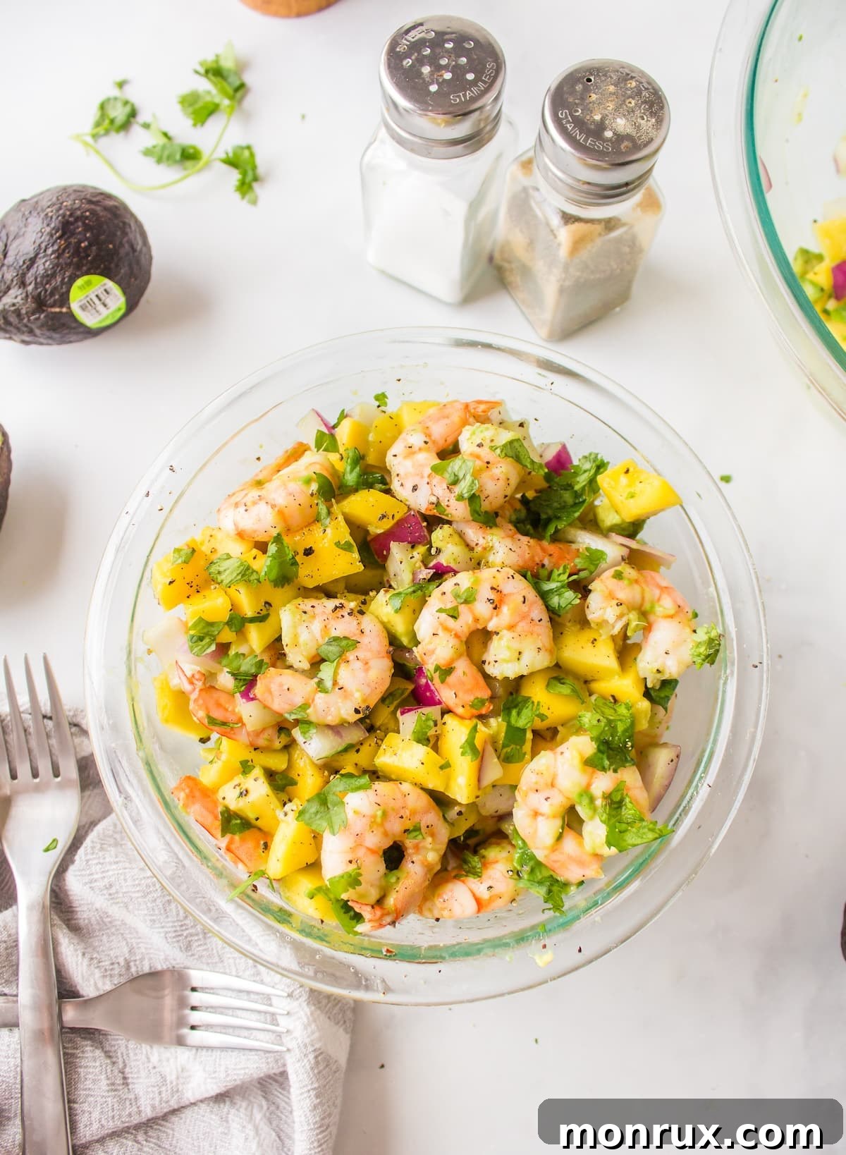 a bowl of avocado mango shrimp salad, garnished with fresh herbs.