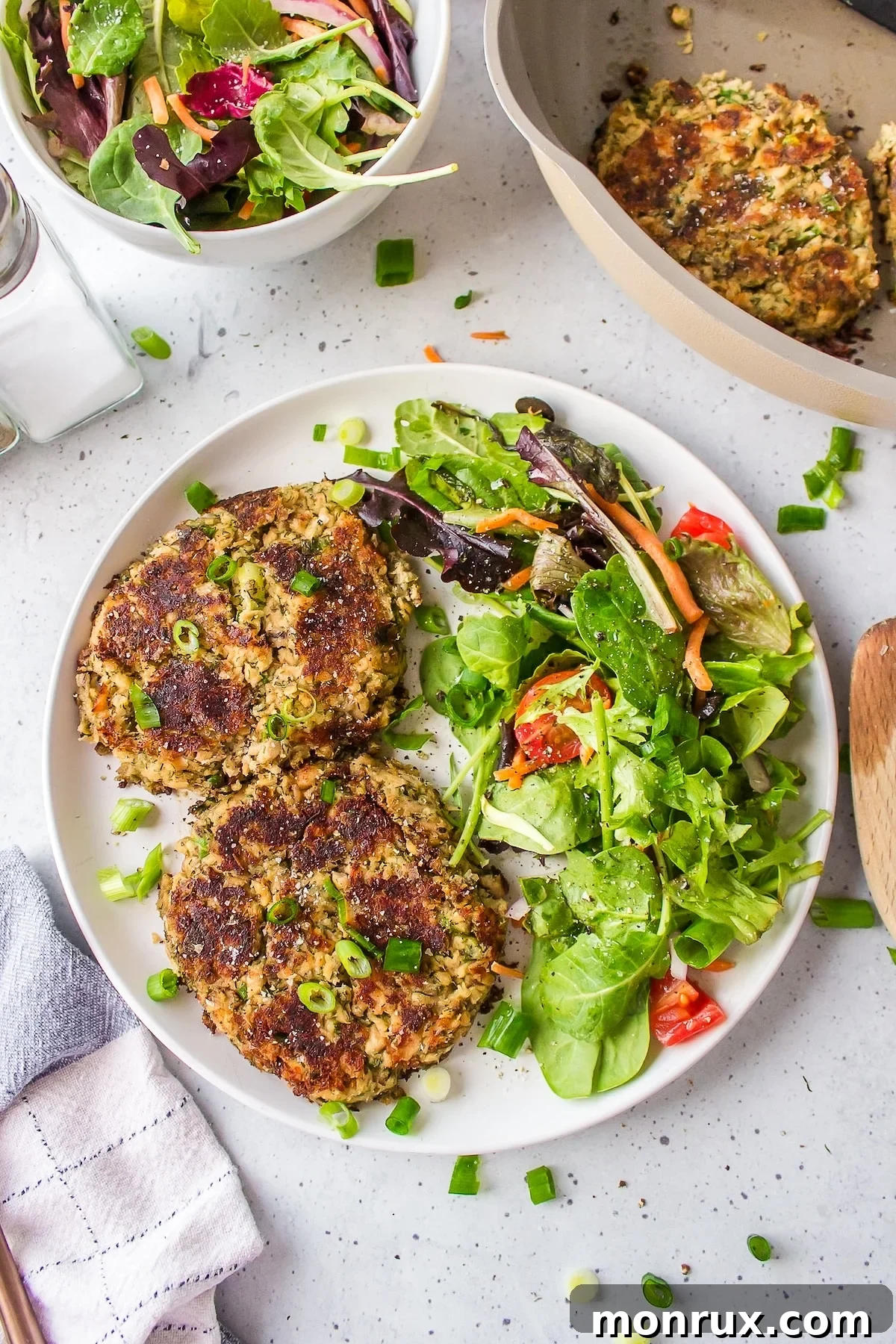 Golden-brown gluten-free salmon cakes on a white plate, served with a fresh green salad.