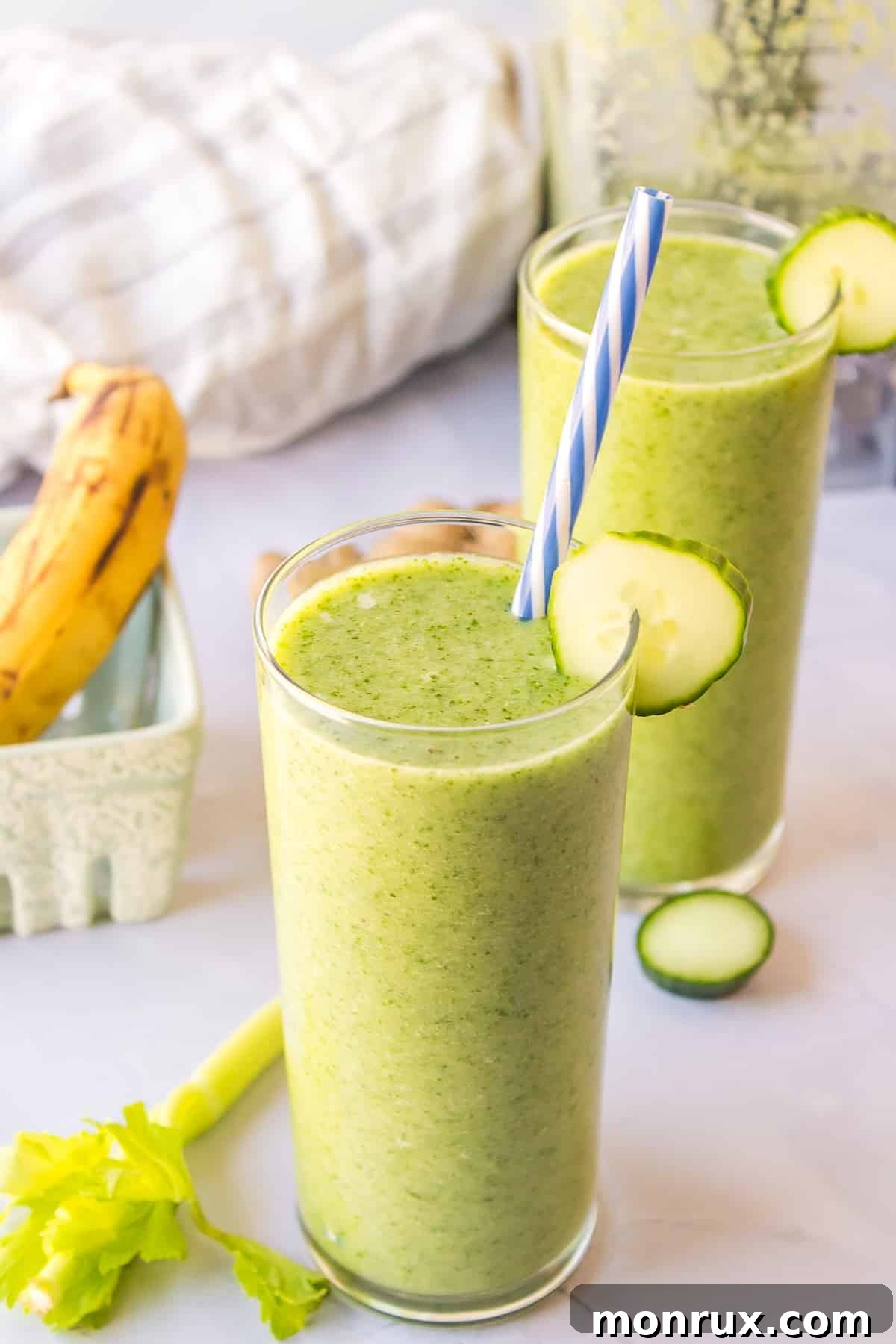 Two glasses of fresh, vibrant green celery cucumber smoothie, garnished with a celery stalk.