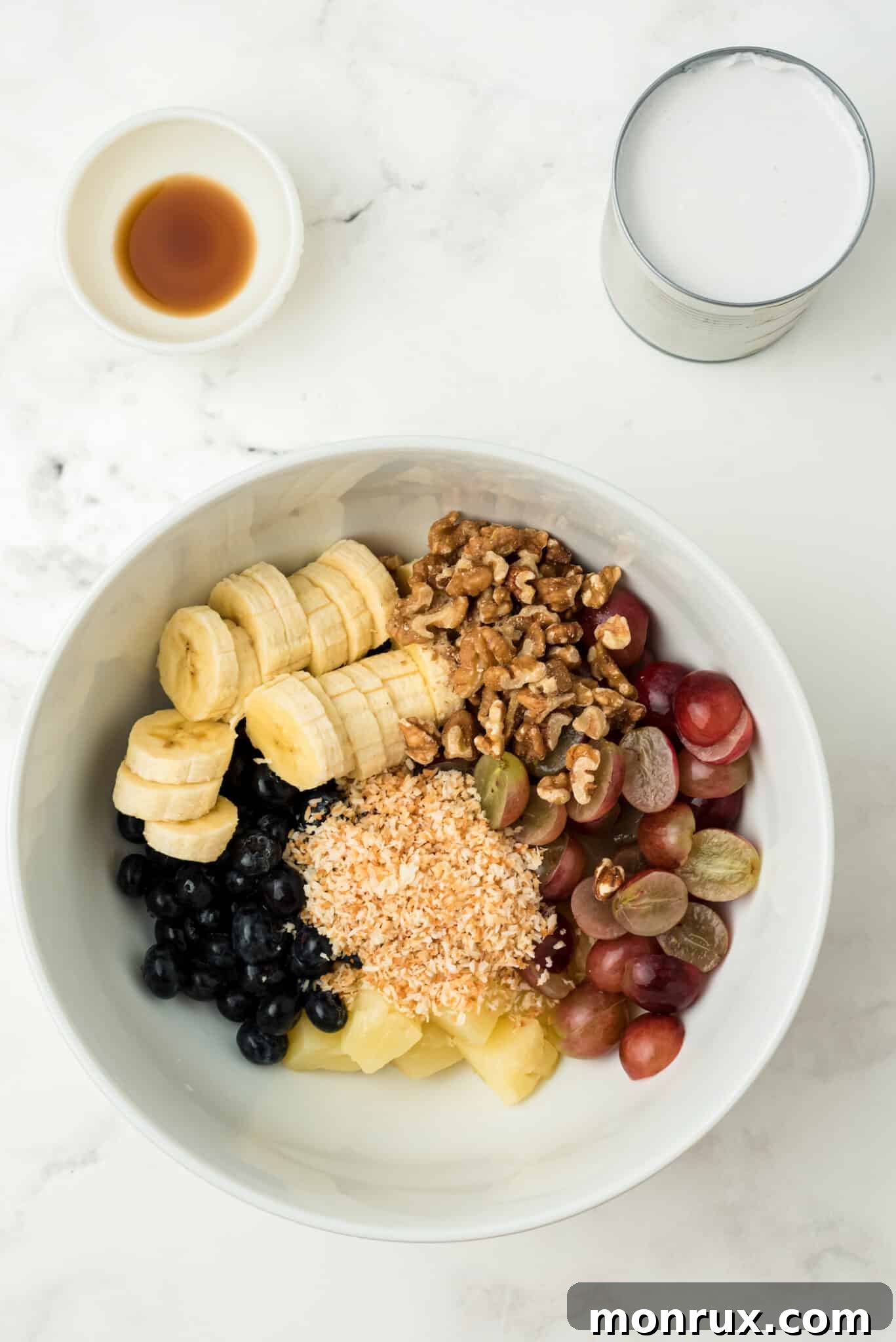 A large mixing bowl filled with colorful fresh fruits and chopped walnuts, ready for the dressing.