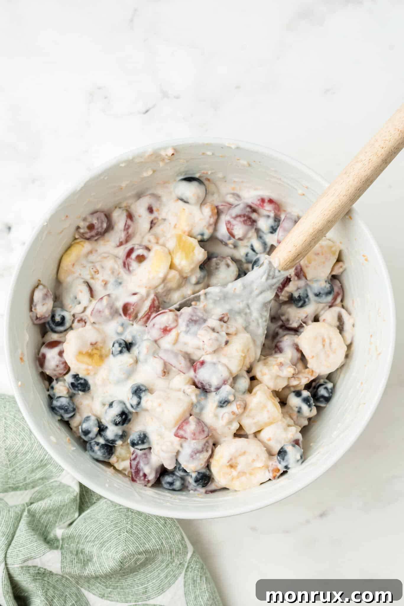 The vibrant fruit and nut mixture being gently folded with the freshly whipped dairy-free coconut cream dressing.