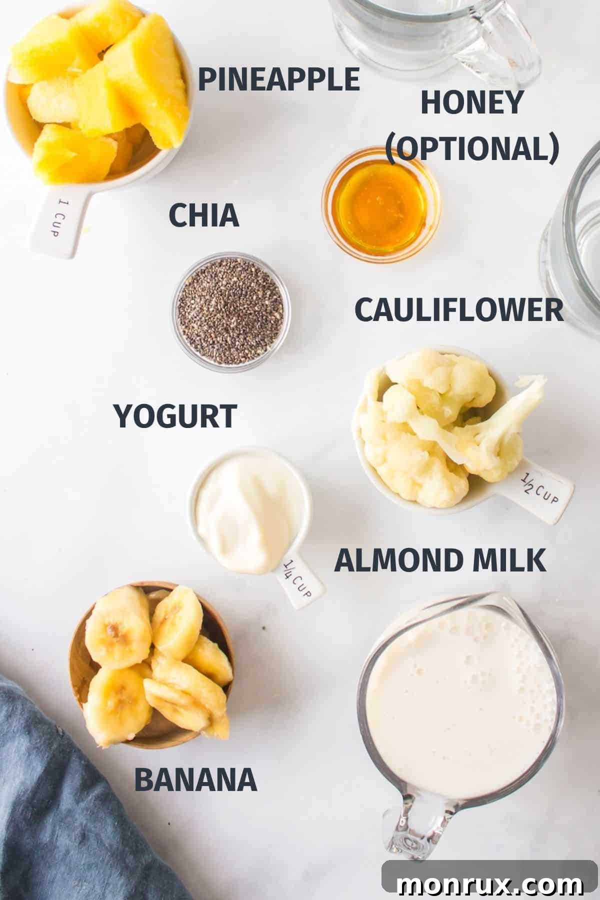Collection of fresh ingredients for a pineapple smoothie recipe, including almond milk, yogurt, pineapple, banana, cauliflower, and chia seeds.