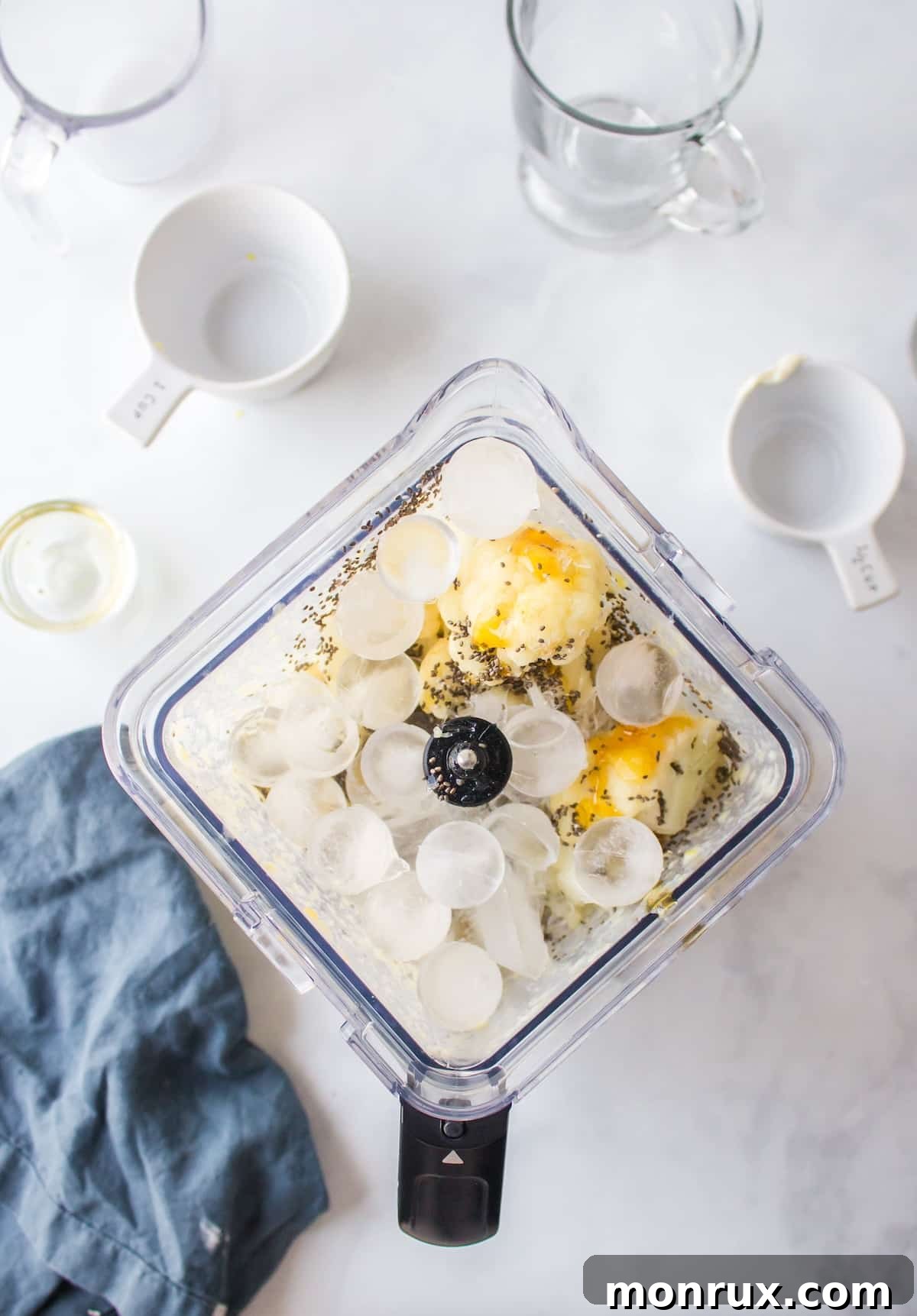 Frozen cauliflower, chia seeds, honey, and ice cubes being added to the blender with other smoothie ingredients.