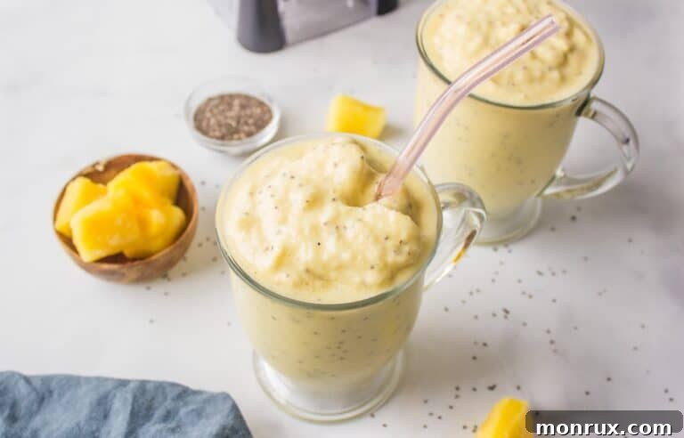 Pineapple smoothie in a glass with a straw, surrounded by fresh ingredients like pineapple chunks and cauliflower florets.