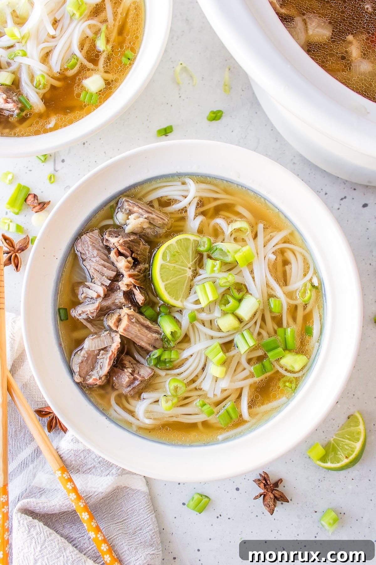 Slow cooker beef pho served in a pristine white bowl, garnished with fresh herbs and a lime wedge.