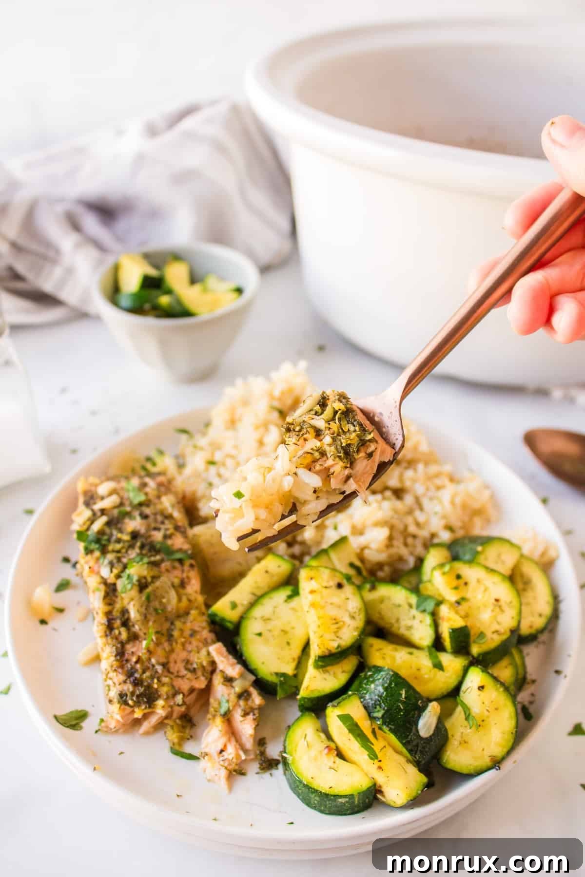 A fork lifts a tender bite of crockpot salmon from a plate, showing its flaky texture, alongside fluffy rice.