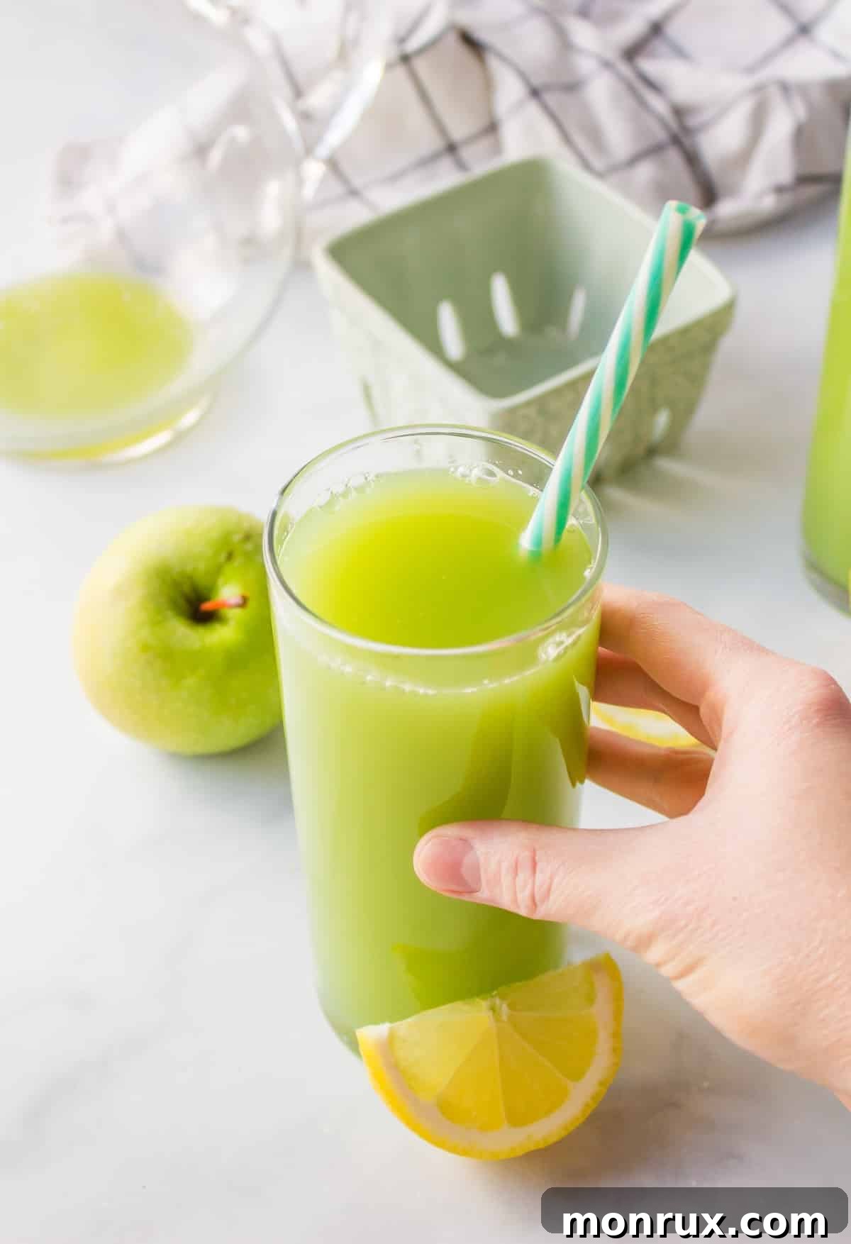 hand reaching for tall glass of pretty green juice with fresh lemon wedge.