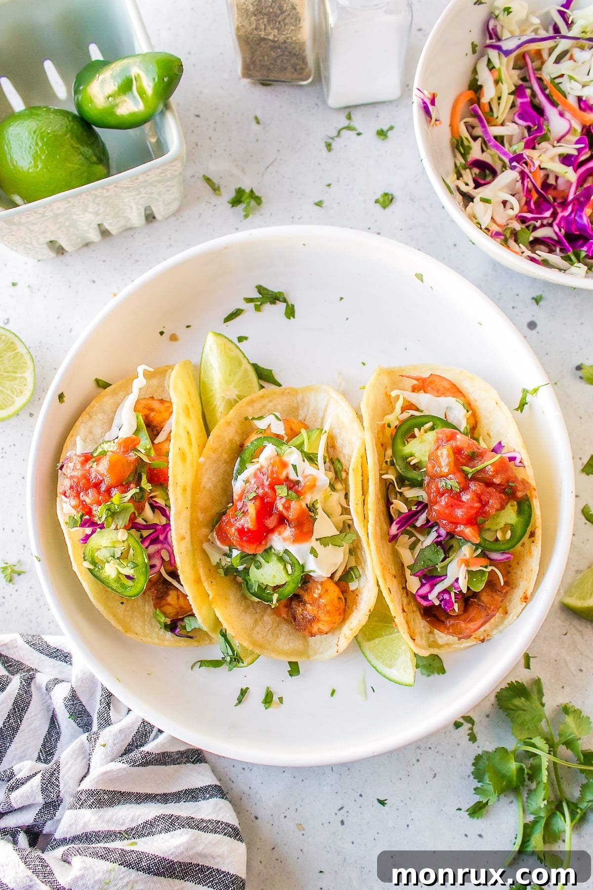 A vibrant plate featuring three Baja shrimp tacos, garnished with fresh cabbage slaw and a squeeze of lime.