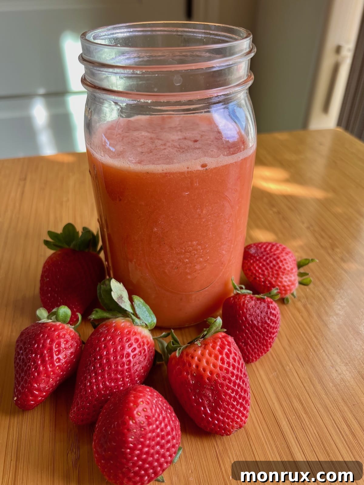 A glass jar filled with freshly made strawberry orange juice, garnished with mint and a slice of orange, invitingly placed on a rustic table.