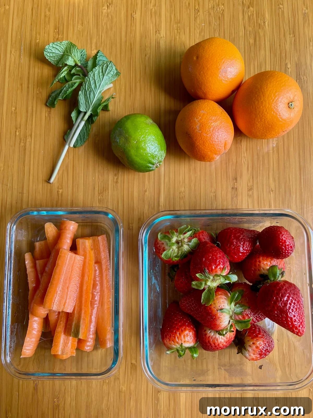 Fresh ingredients for strawberry orange juice including strawberries, oranges, carrots, limes, and mint leaves arranged on a cutting board.