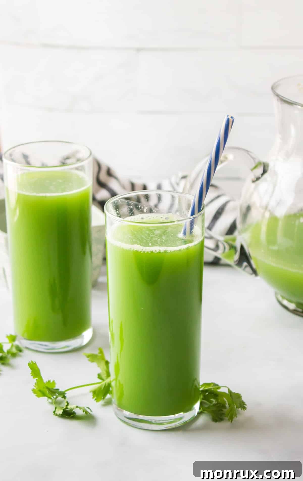 Two glasses of refreshing green cilantro juice with straws, ready to drink.