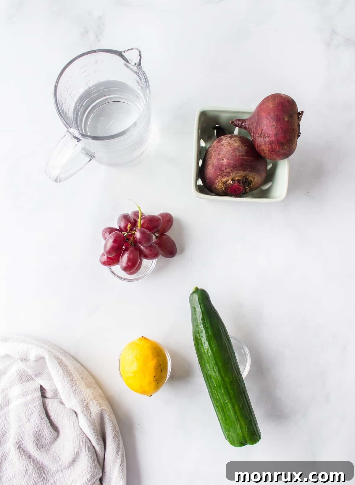 Fresh ingredients laid out on a wooden table, including raw beets, purple grapes, cucumber, and a lemon, ready for making a healthy purple juice.