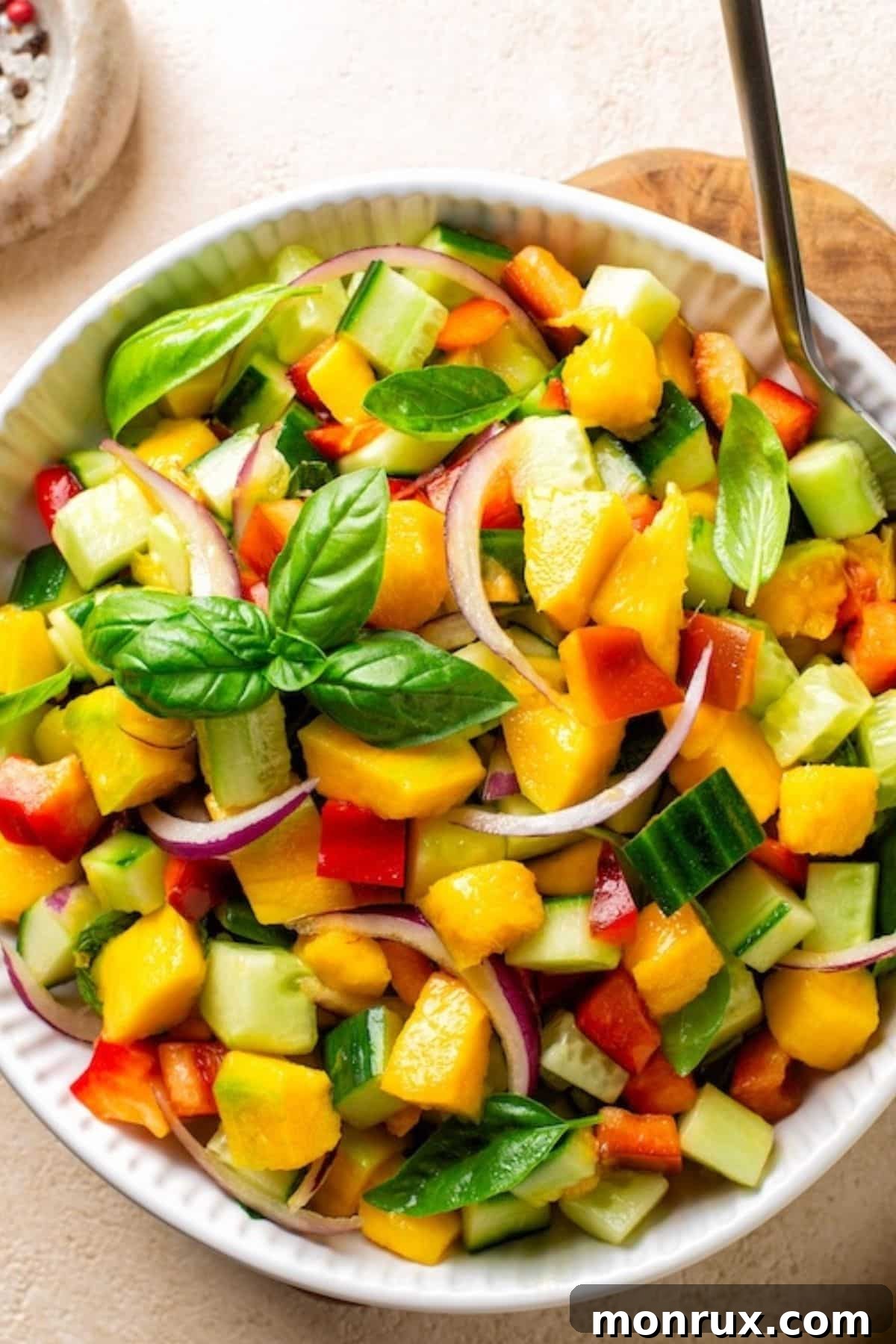 A bowl brimming with a colorful Bell Pepper Cucumber Mango Salad, garnished with fresh herbs.