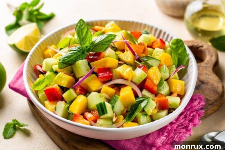 A close-up of a vibrant bell pepper cucumber mango salad with fresh mango and herbs in a white bowl.