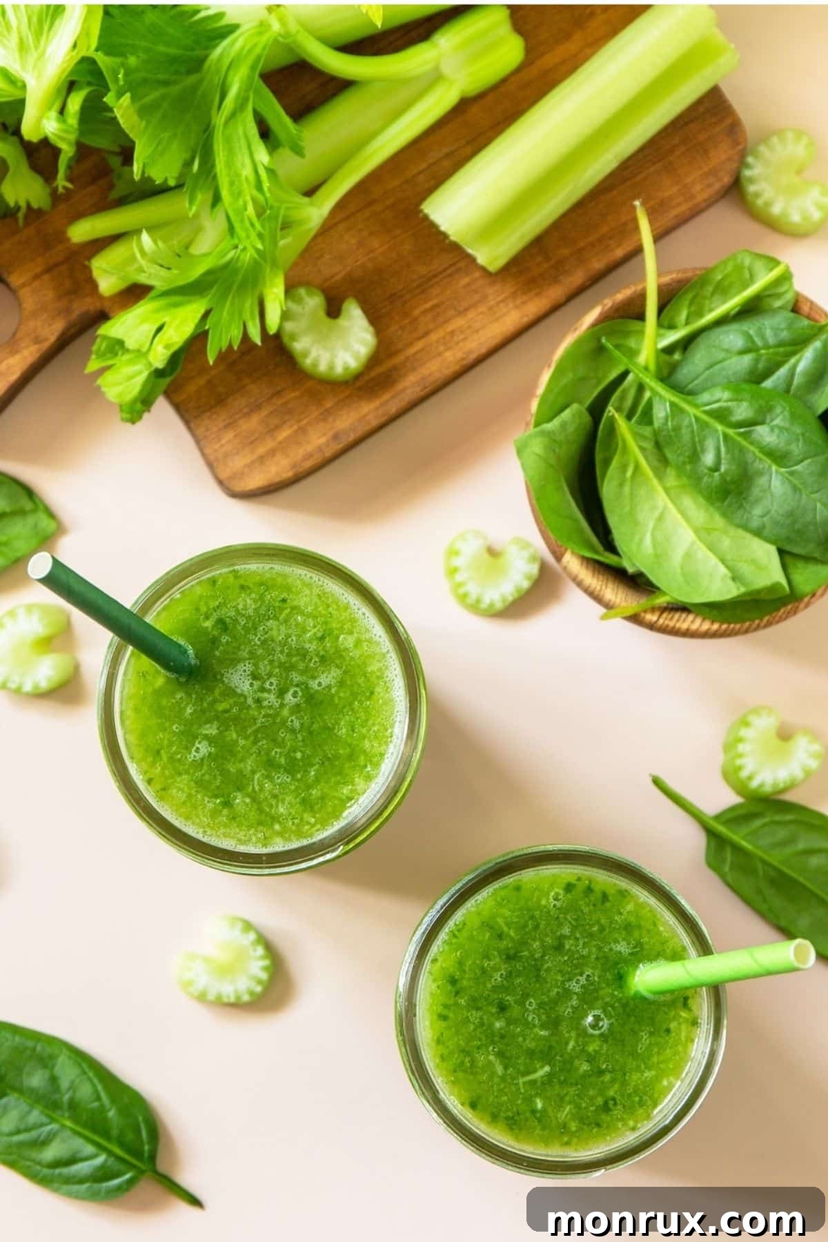Freshly prepared spinach and celery juice in a glass, with ingredients scattered on a table.