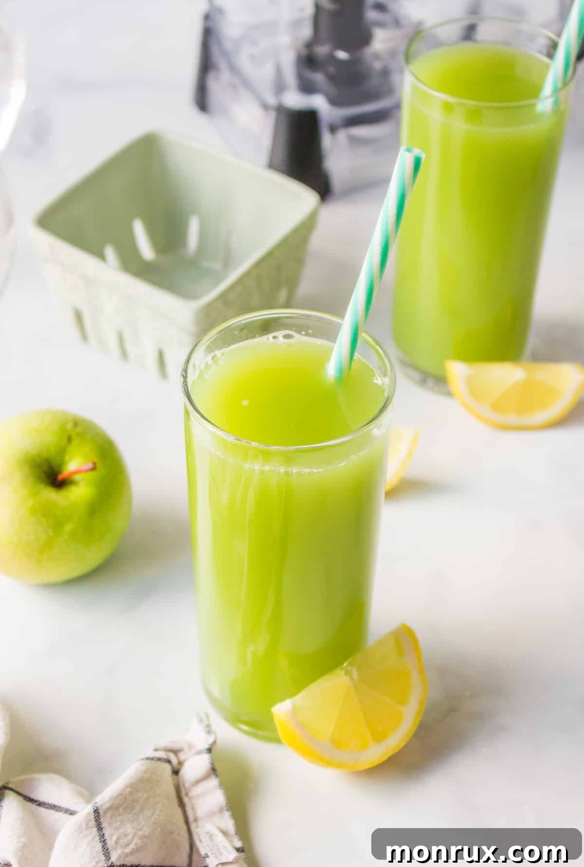 Tall glass of green juice with fresh lemons on table, emphasizing freshness and natural ingredients.