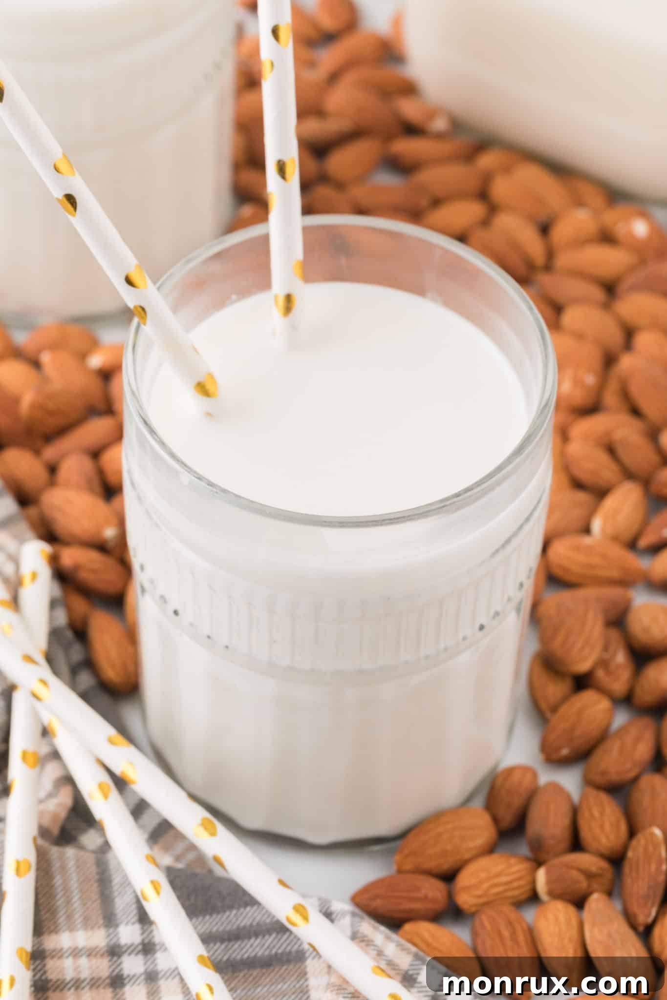 Two glasses of homemade almond milk on a wooden table, surrounded by raw almonds.