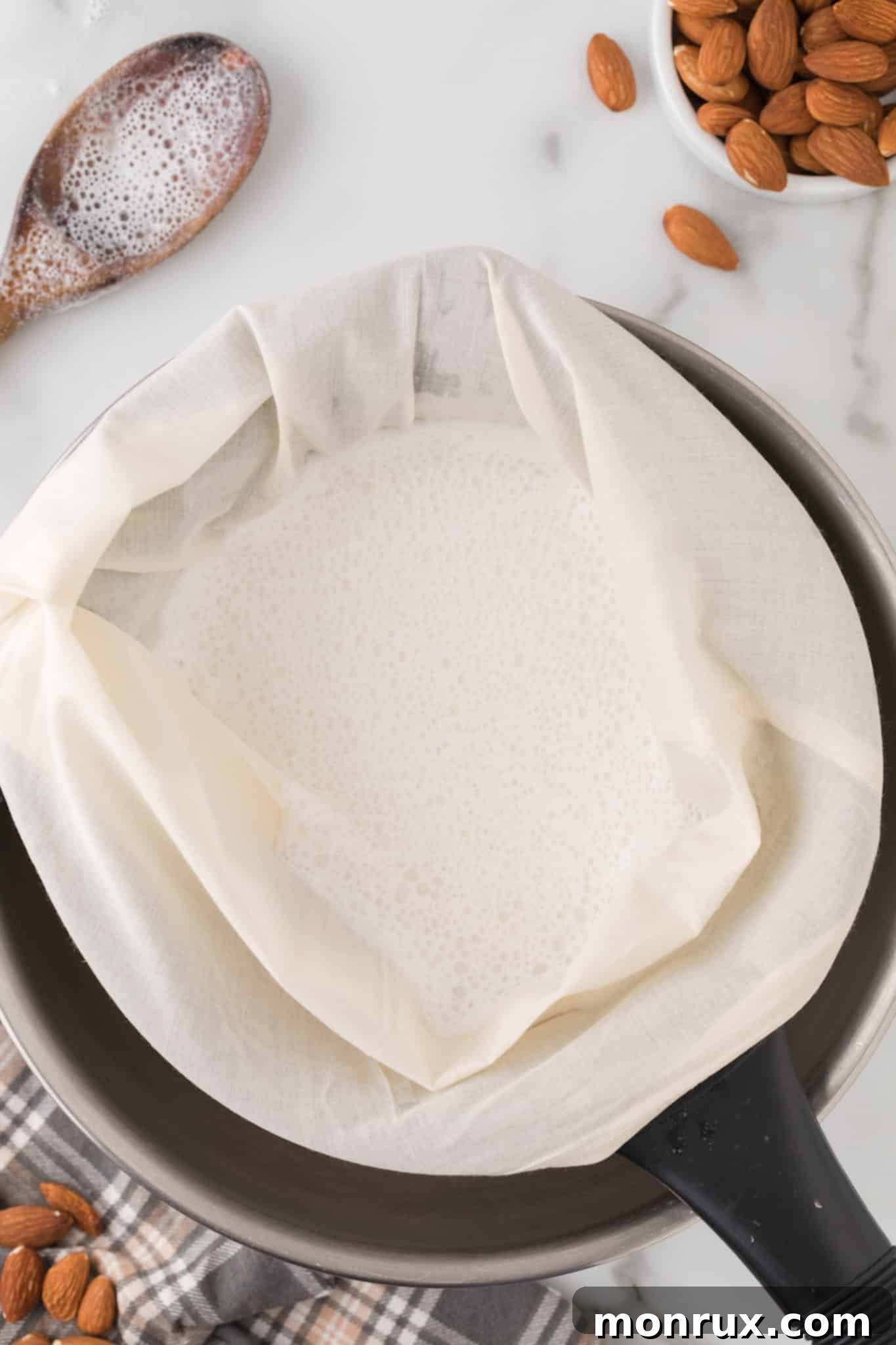 Straining homemade almond milk through a nut milk bag into a bowl.