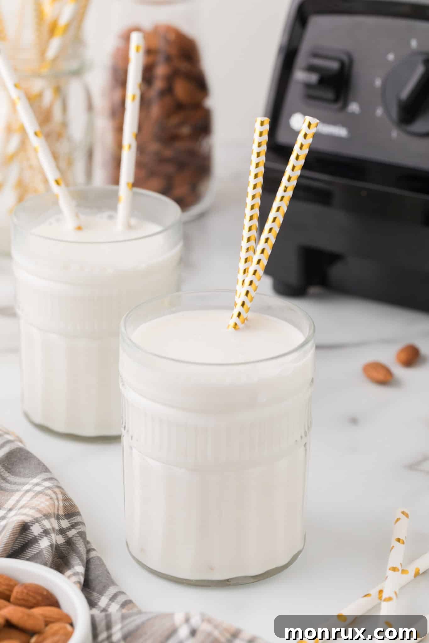 Two glasses of homemade almond milk, each with two paper straws, ready to be enjoyed.