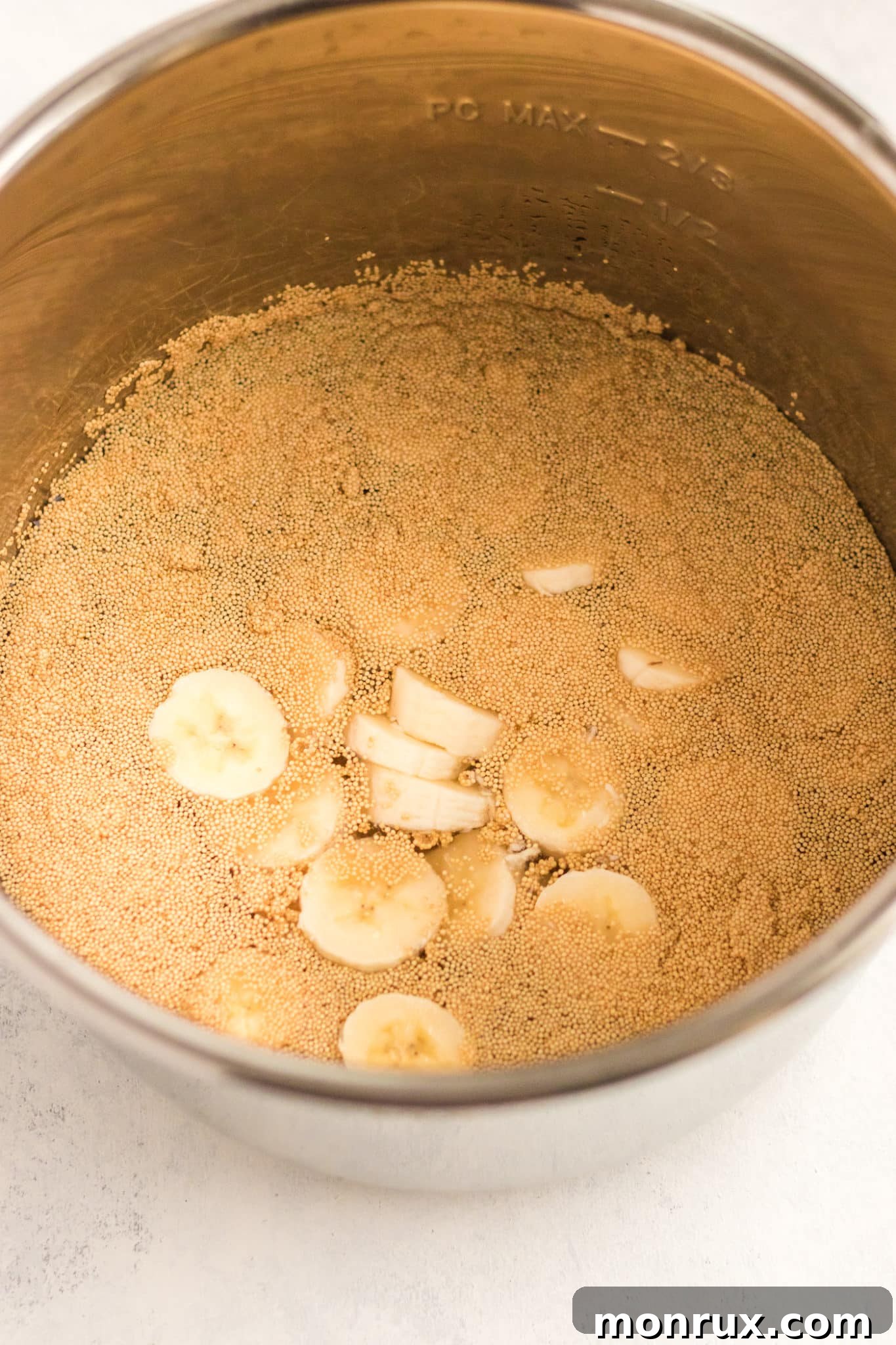 Inside a pressure cooker, uncooked amaranth and sliced bananas are combined with plant-based milk, ready for cooking.